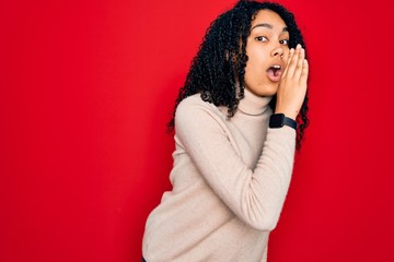Young african american curly woman wearing casual turtleneck sweater over red background hand on mouth telling secret rumor, whispering malicious talk conversation