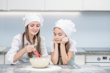 Mother teaches her little daughter to cook dough in the kitchen at home