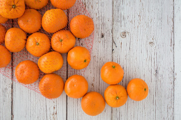 Small clementine oranges spilling from a red mesh bag onto a whitewashed wood background
