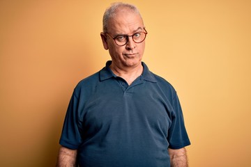 Middle age handsome hoary man wearing casual polo and glasses over yellow background skeptic and...