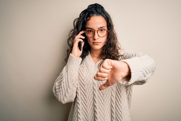Young beautiful woman with curly hair having conversation talking on the smartphone with angry face, negative sign showing dislike with thumbs down, rejection concept