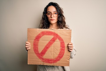 Young beautiful woman with curly hair holding banner with prohibited signal message with a...