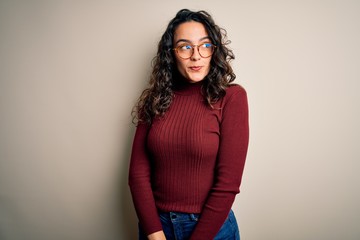 Beautiful woman with curly hair wearing casual sweater and glasses over white background smiling looking to the side and staring away thinking.