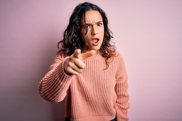 Young beautiful woman with curly hair wearing casual sweater over isolated pink background pointing displeased and frustrated to the camera, angry and furious with you