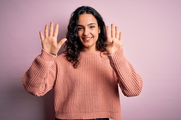 Young beautiful woman with curly hair wearing casual sweater over isolated pink background showing...