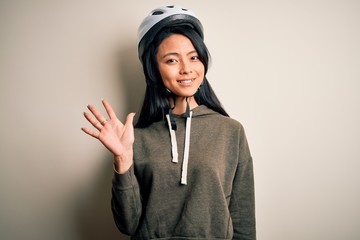 Young beautiful chinese woman wearing bike helmet over isolated white background showing and pointing up with fingers number five while smiling confident and happy.