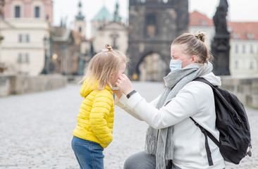 Mother puts on her little daughter a protective medical mask on Charles Bridge in Prague....