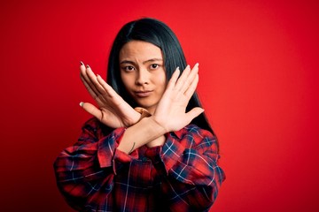 Young beautiful chinese woman wearing casual shirt over isolated red background Rejection expression crossing arms doing negative sign, angry face