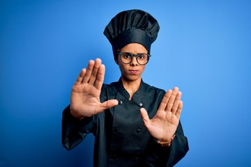 Young african american chef woman wearing cooker uniform and hat over blue background doing stop gesture with hands palms, angry and frustration expression