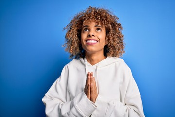 Beautiful african american sporty woman wearing casual sweatshirt over blue background begging and...