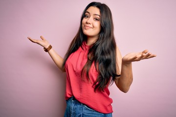 Young brunette woman wearing casual summer shirt over pink isolated background clueless and...