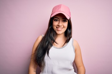 Young brunette woman wearing casual sport cap over pink background with a happy and cool smile on face. Lucky person.