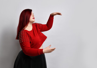 Plus size ginger girl in red spiked top, black leather skirt. Looking surprised, holding something...