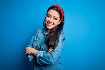 Young brunette woman wearing casual denim shirt over blue isolated background happy face smiling with crossed arms looking at the camera. Positive person.