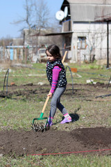 a little white dark-haired white girl with a ponytail outdoors holds a long wooden stick in her hands. Preschooler helps parents in the spring garden