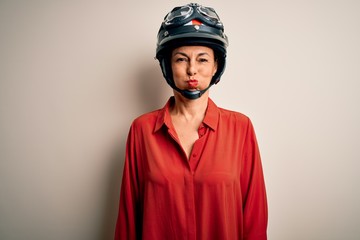 Middle age motorcyclist woman wearing motorcycle helmet over isolated white background puffing cheeks with funny face. Mouth inflated with air, crazy expression.
