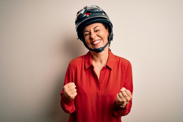 Middle age motorcyclist woman wearing motorcycle helmet over isolated white background very happy and excited doing winner gesture with arms raised, smiling and screaming for success. Celebration
