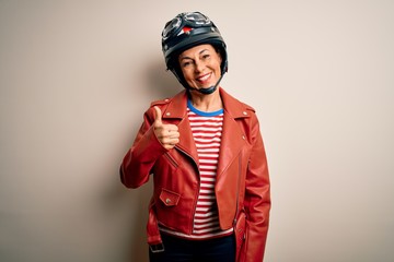 Middle age motorcyclist woman wearing motorcycle helmet and jacket over white background doing happy thumbs up gesture with hand. Approving expression looking at the camera showing success.