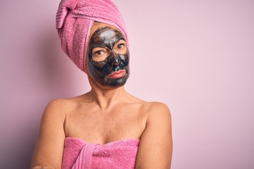 Middle age brunette woman wearing beauty black face mask over isolated pink background skeptic and nervous, disapproving expression on face with crossed arms. Negative person.