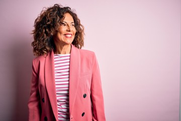 Middle age beautiful businesswoman wearing elegant jacket over isolated pink background looking...