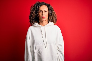 Middle age beautiful sporty woman wearing white sweatshirt over isolated red background with...