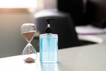 hand alcohol gel sanitizer dispenser and Hourglass on table, against Novel coronavirus or Corona Virus Disease (Covid-19) at office or home .Hygiene, Health and time to stop pandemic concept