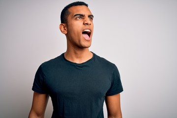 Young handsome african american man wearing casual t-shirt standing over white background angry and mad screaming frustrated and furious, shouting with anger. Rage and aggressive concept.