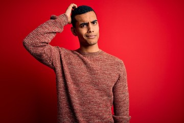 Young handsome african american man wearing casual sweater standing over red background confuse and wonder about question. Uncertain with doubt, thinking with hand on head. Pensive concept.