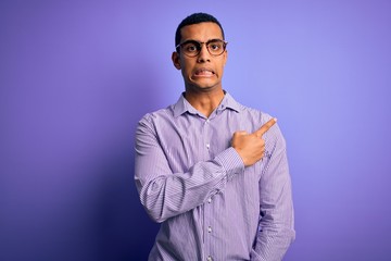 Handsome african american man wearing striped shirt and glasses over purple background Pointing aside worried and nervous with forefinger, concerned and surprised expression