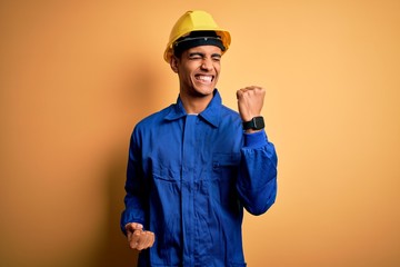 Young handsome african american worker man wearing blue uniform and security helmet celebrating...