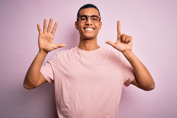 Handsome african american man wearing casual t-shirt and glasses over pink background showing and pointing up with fingers number seven while smiling confident and happy.