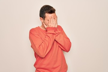 Young handsome man with blue eyes wearing casual sweater standing over white background with sad expression covering face with hands while crying. Depression concept.