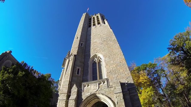 Camera trucks around gothic bell tower with autumn trees.