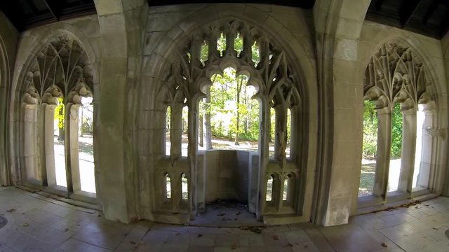 Steadicam shot entering gothic cloisters and moving to balcony with view of lawn and trees.