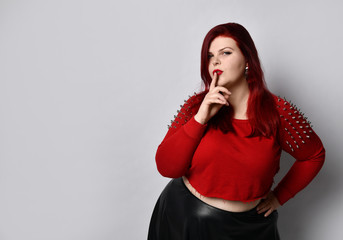 Overweight redhead woman in red spiked top, black leather skirt. Touching face, put hand on hip,...
