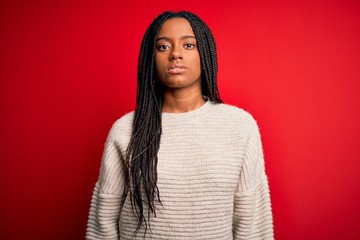 Fototapeta premium Young african american woman wearing casual winter sweater over red isolated background Relaxed with serious expression on face. Simple and natural looking at the camera.