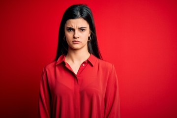 Fototapeta premium Young beautiful brunette woman wearing casual shirt standing over red background skeptic and nervous, frowning upset because of problem. Negative person.