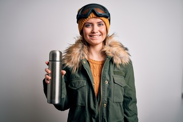 Young beautiful skier woman with blue eyes wearing ski goggles drinking thermo with coffee with a...