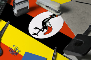Uganda flag with office clerk workplace background. National stationary concept with office tools.