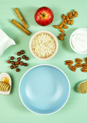 Healthy breakfast preparation creative composition concept with oats, spices, yogurt, fresh fruit, nuts, honey and high fiber LSA on modern green background. Top view flatlay vertical.