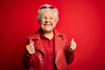 Senior beautiful grey-haired woman wearing casual red jacket and sunglasses excited for success...