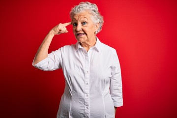 Senior beautiful woman wearing elegant shirt standing over isolated red background Smiling pointing to head with one finger, great idea or thought, good memory