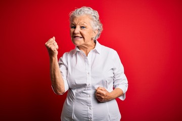 Senior beautiful woman wearing elegant shirt standing over isolated red background celebrating surprised and amazed for success with arms raised and eyes closed. Winner concept.