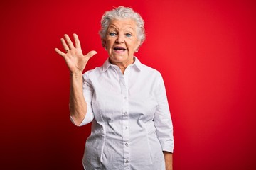 Senior beautiful woman wearing elegant shirt standing over isolated red background showing and pointing up with fingers number five while smiling confident and happy.