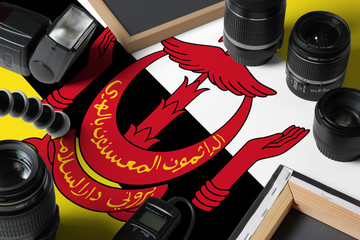 Brunei national flag with top view of personal photographer equipment and tools on white wooden table, copy space.