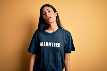 Young beautiful hispanic woman wearing volunteer t-shirt as social charity moral looking sleepy and...