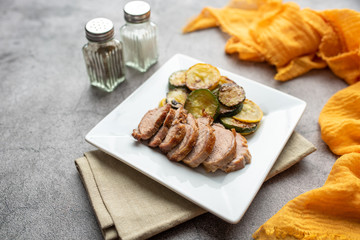 Sliced roast pork on a plate with zucchini and squash circles 