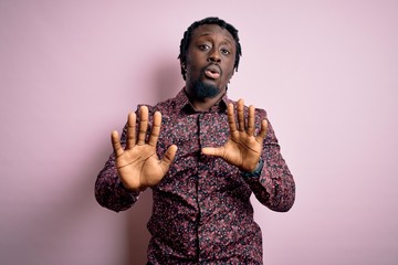 Young handsome african american man wearing casual shirt standing over pink background Moving away hands palms showing refusal and denial with afraid and disgusting expression. Stop and forbidden.