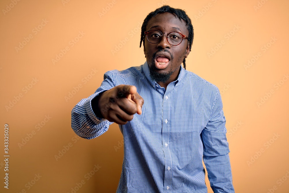 Wall mural Young handsome african american man wearing shirt and glasses over yellow background pointing displeased and frustrated to the camera, angry and furious with you