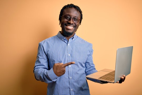 Young african american worker man working using laptop standing over yellow background very happy pointing with hand and finger